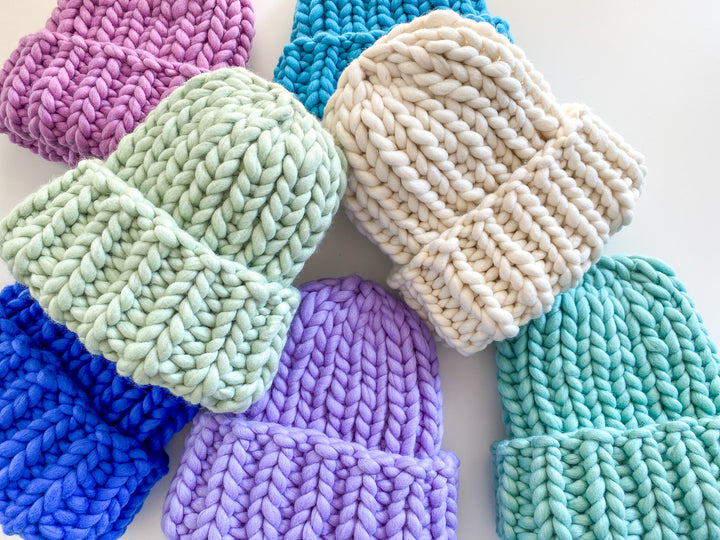 Colorful knitted chunky beanies in various shades on a white background