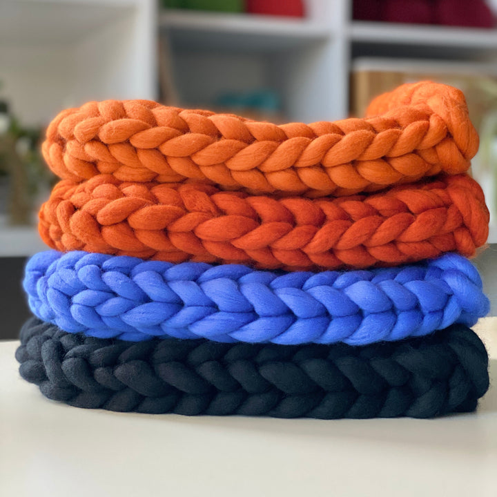 Chunky knit beanies in orange shades, blue, and black on a white surface.