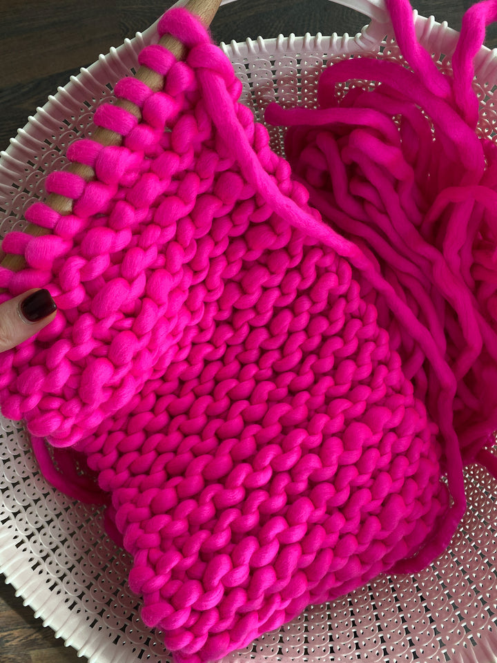 Colorful scarf being hand knitted in bright pink merino wool