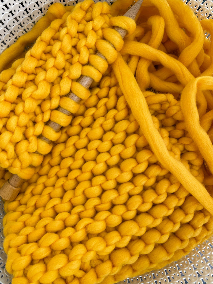 Colorful scarf being hand knitted with bright yellow merino wool and wooden knitting needles.