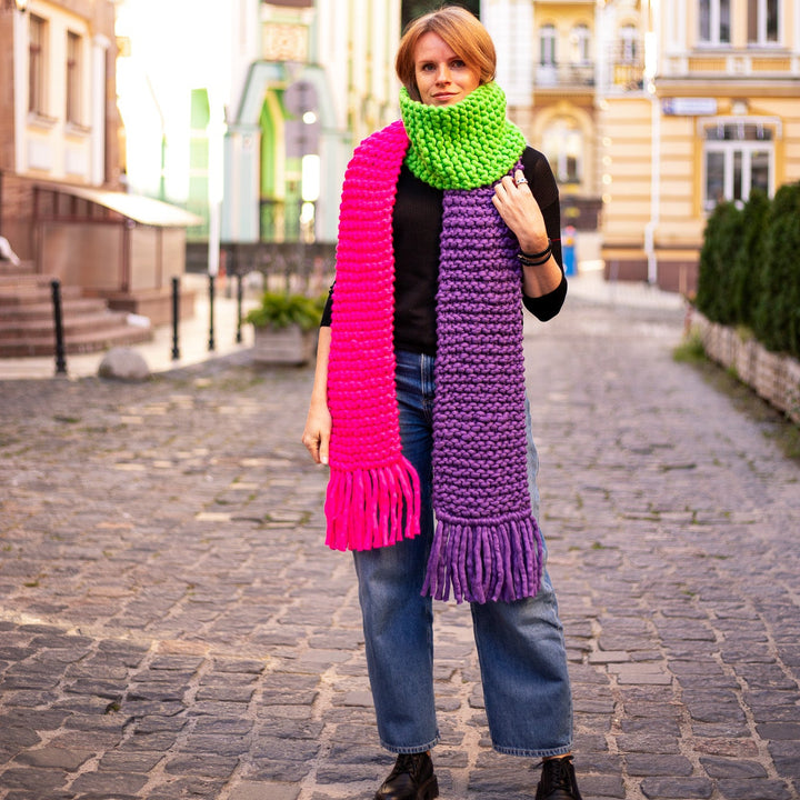 Colorful scarf with fringes, hand knitted from Italian merino wool, showcased by a model on a cobblestone street.