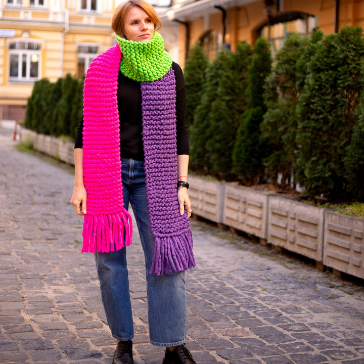 Colorful scarf with fringes in pink, green, and purple worn by a woman outdoors.