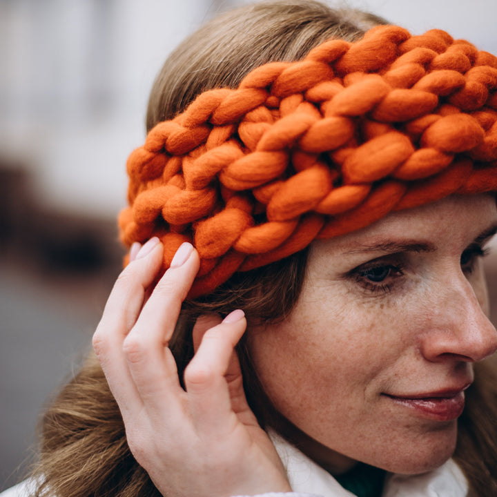 Person wearing an orange knitted headband with a blurred background